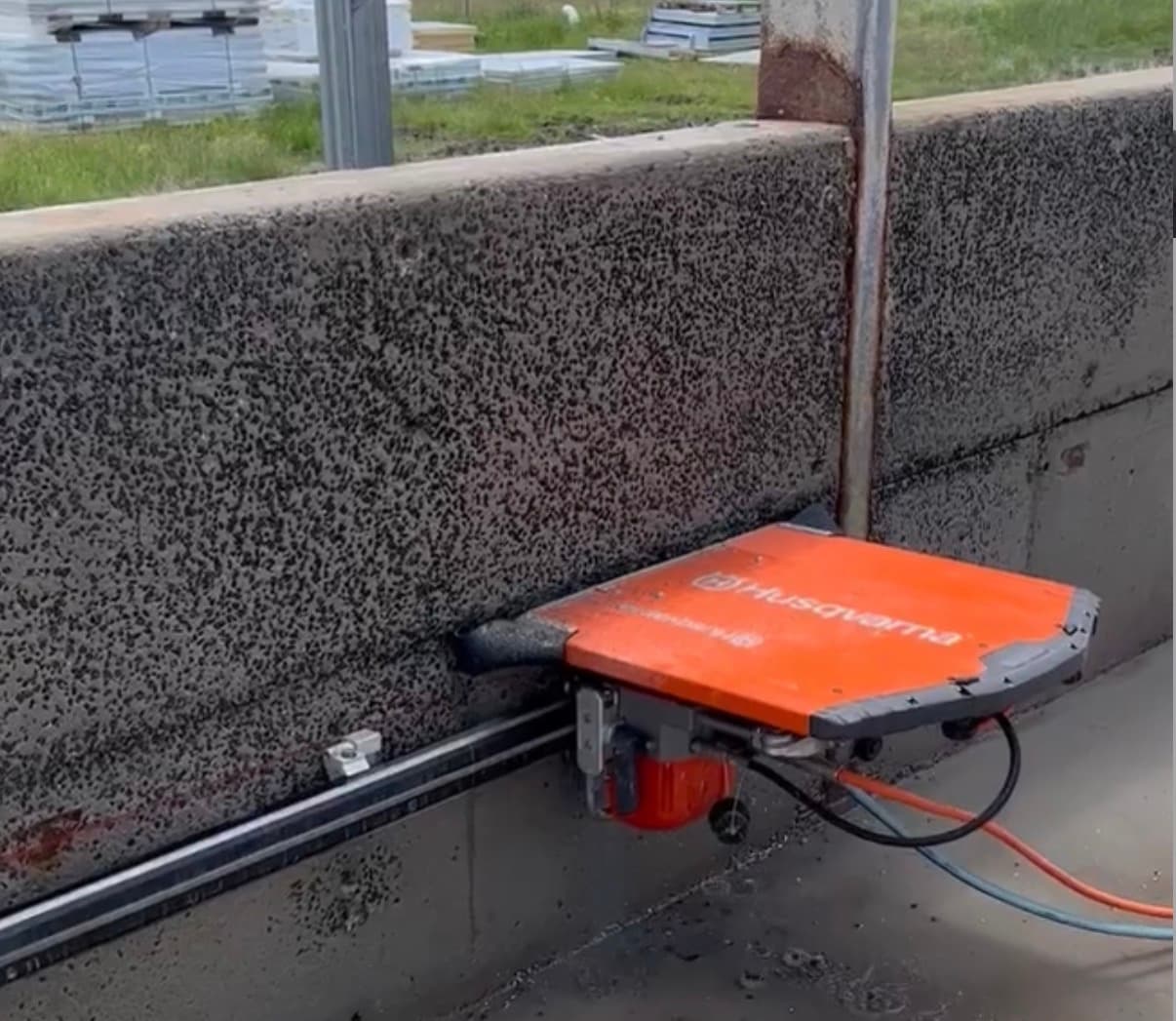 Orange Husqvarna wall saw on a rail cutting into a thick, textured concrete wall.