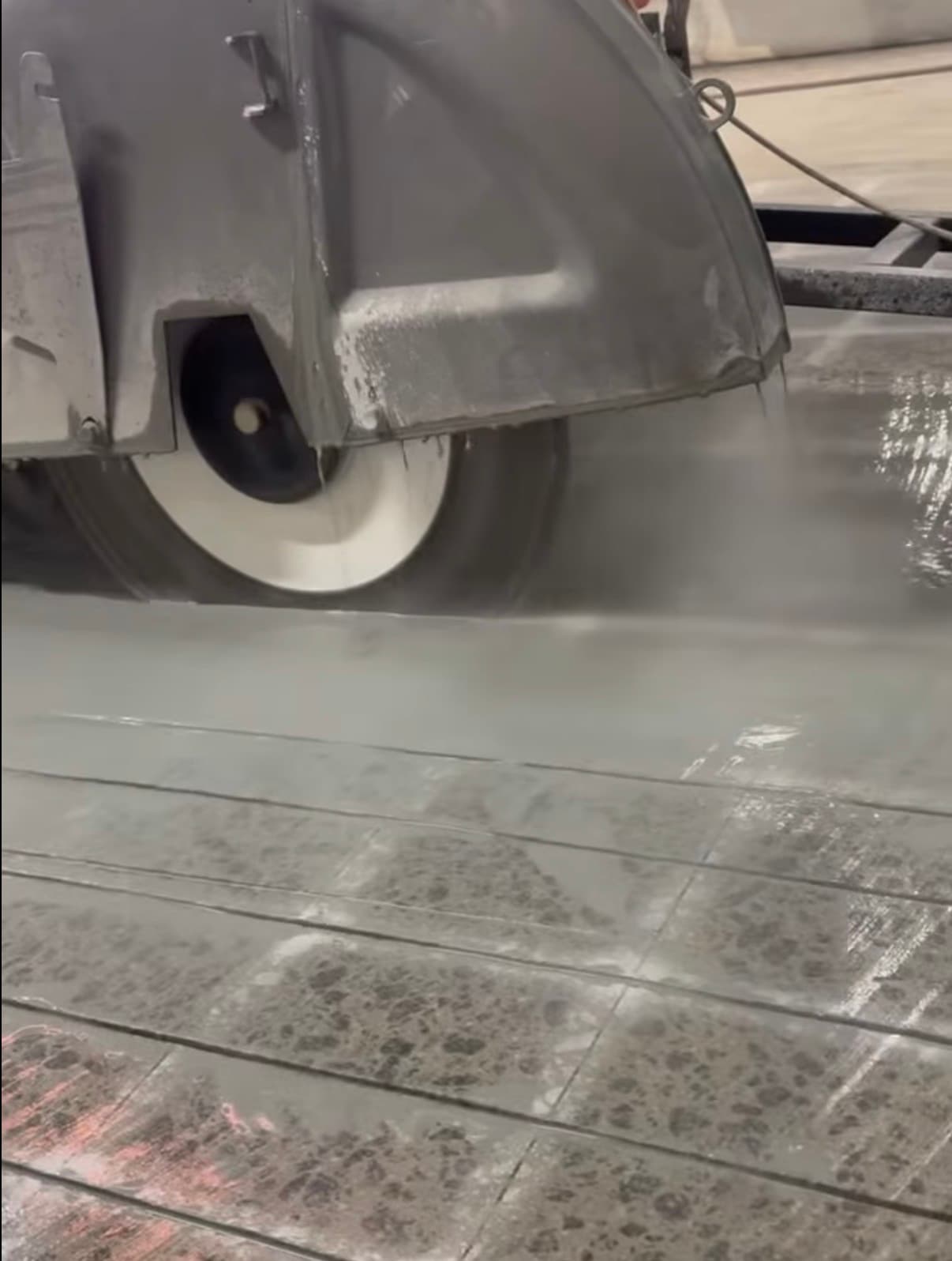 Industrial concrete saw cutting into a wet floor with water spray for dust suppression.