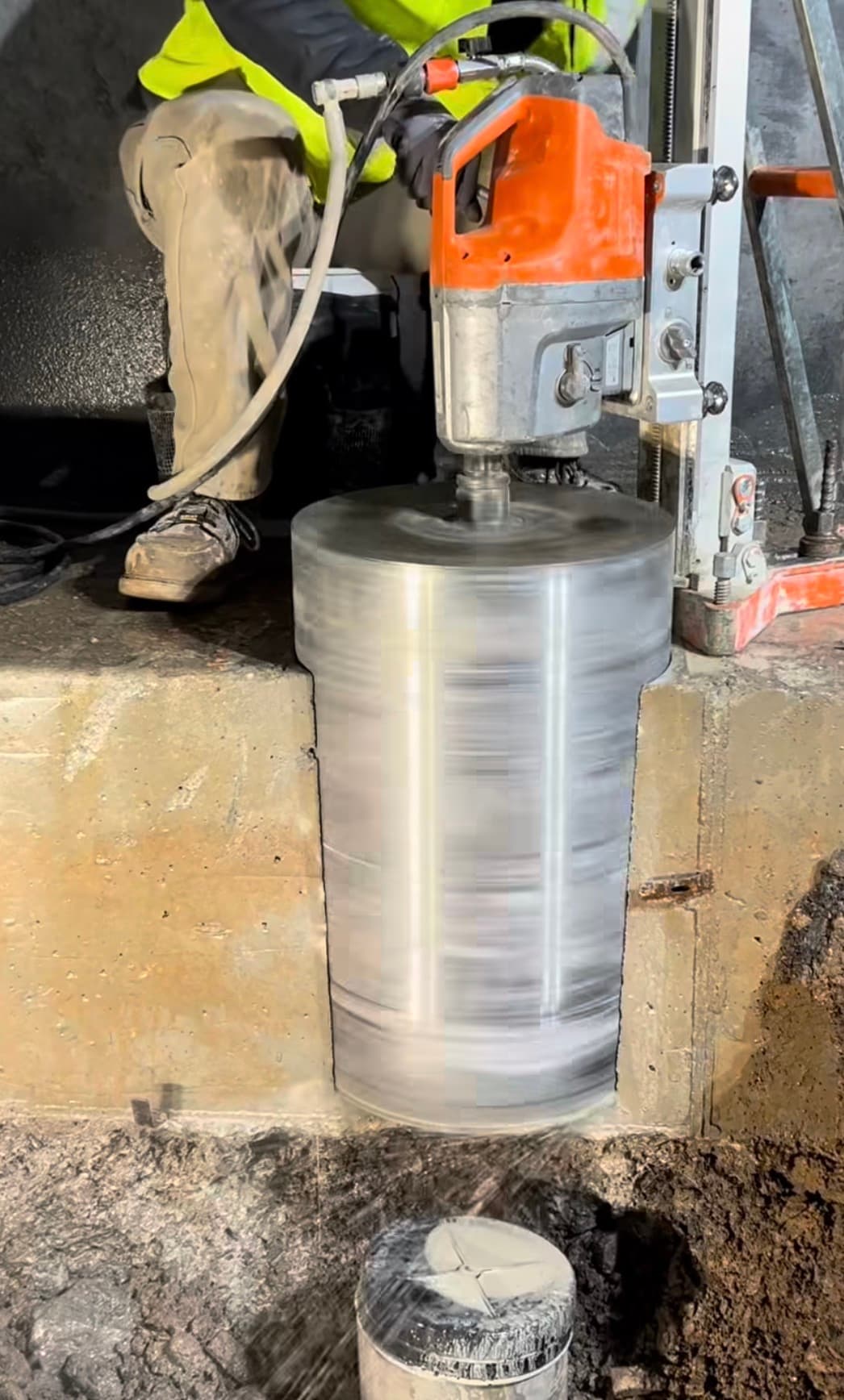 Orange core drill machine boring a large cylindrical hole into a thick concrete slab.