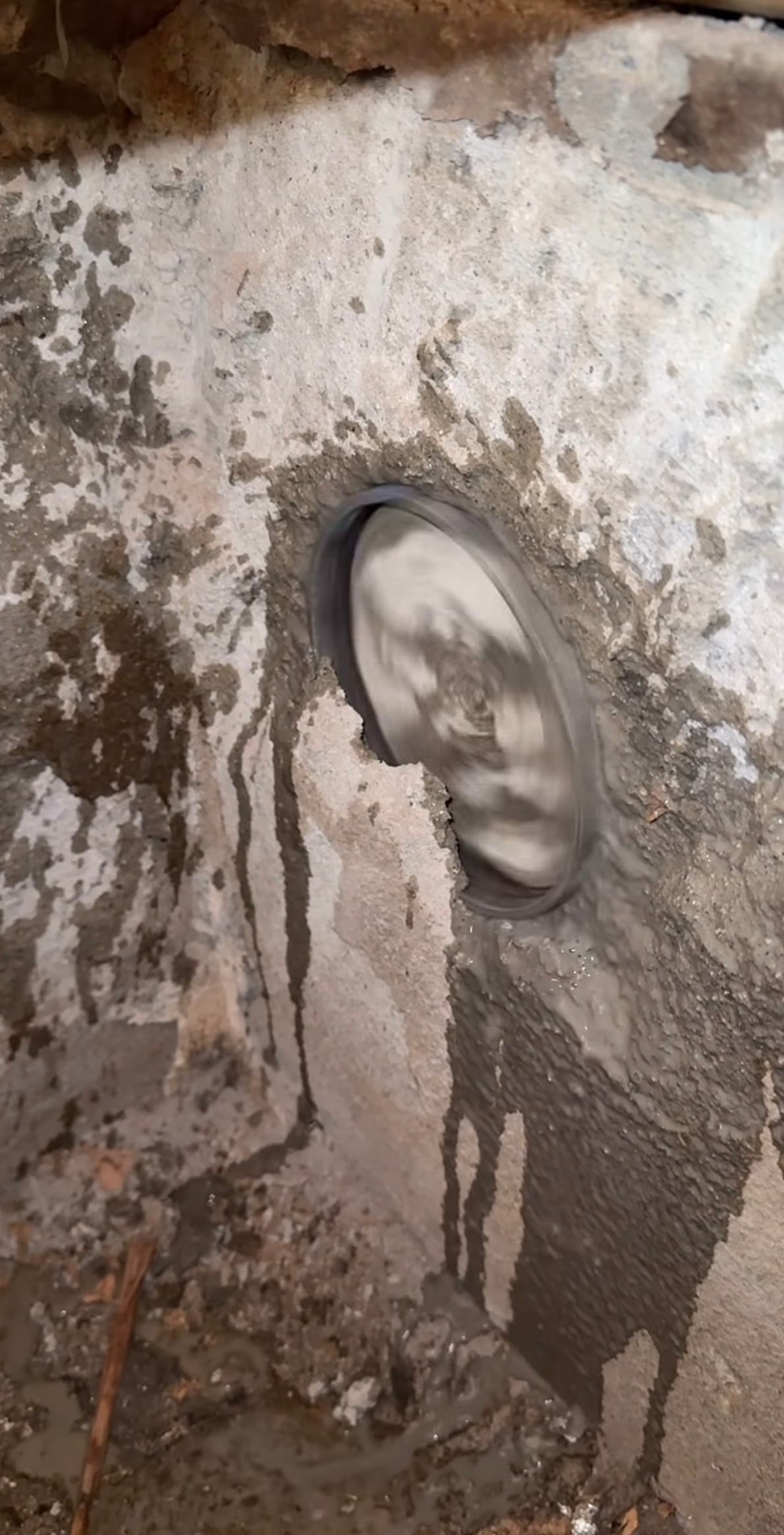 Spinning core drill bit cutting a circular hole into a concrete wall with wet slurry.