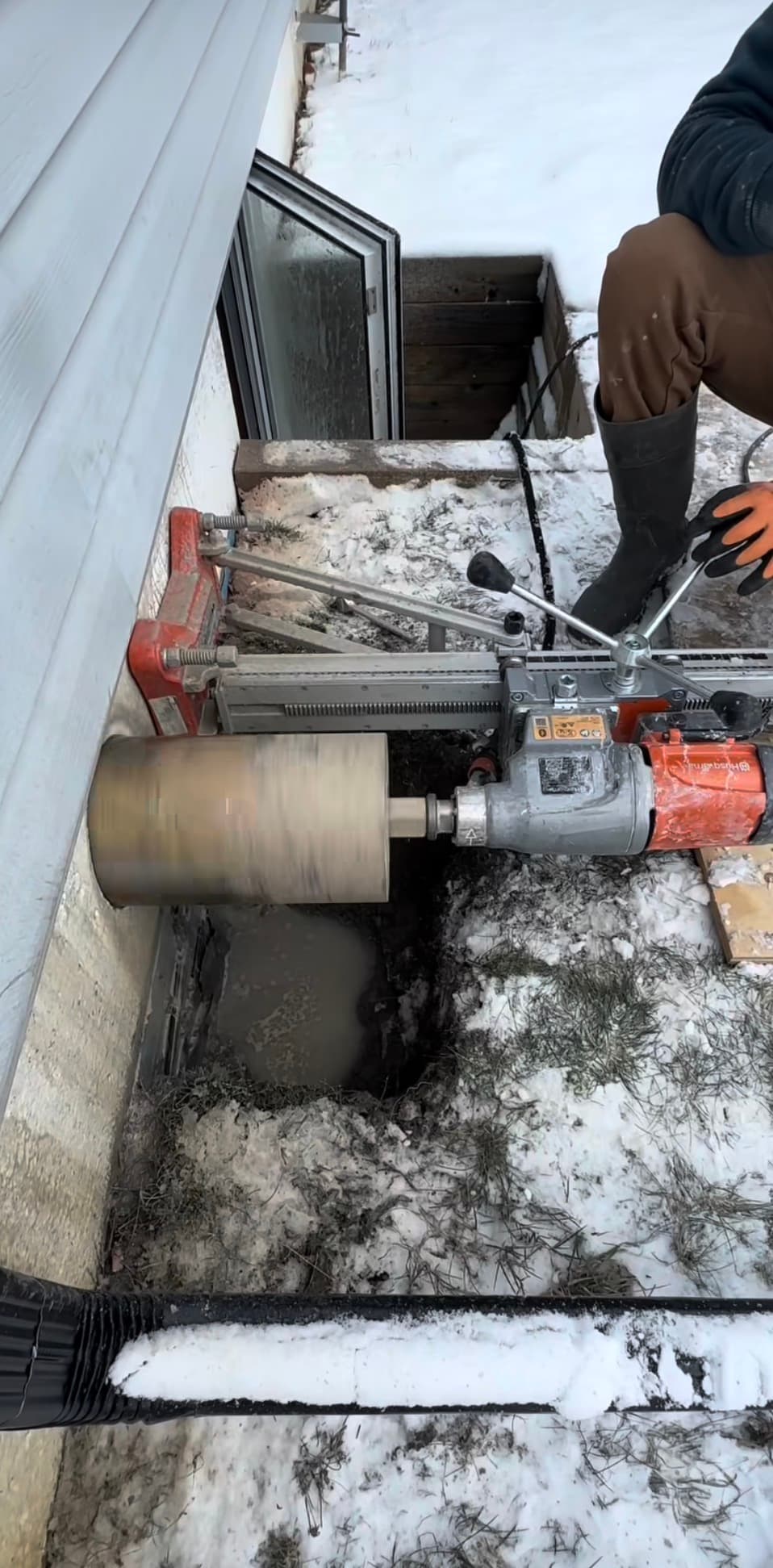 Core drill machine cutting a large hole into a concrete foundation wall in the snow.