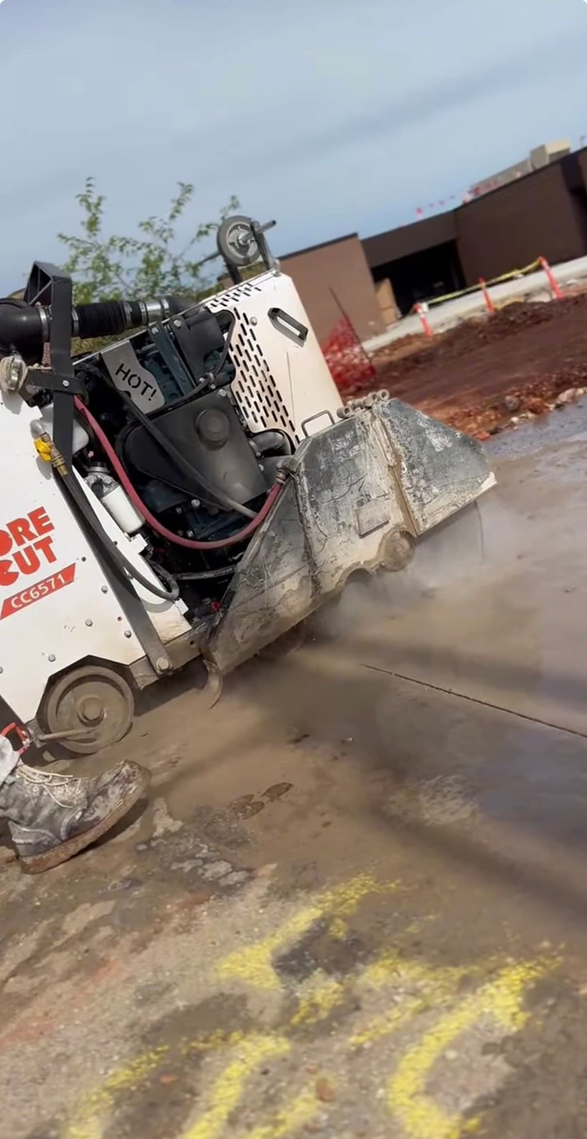 Walk-behind concrete saw cutting a line into wet pavement, creating a spray of water mist.